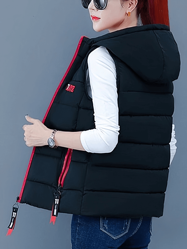 Woman wearing a black women's down vest with red zipper pockets and hood, paired with sunglasses and a white shirt, showing side view.